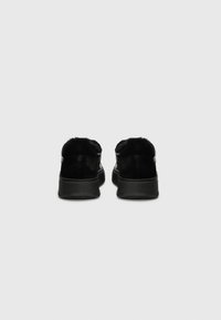 Adidași negri, cu un accent de blană moale pe călcâi, corp din piele netedă și o talpă din cauciu negru texturat. Design simplu și modern.