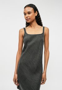 Vestido gris sin mangas con escote cuadrado. La tela suave y texturizada presenta costuras visibles y un corte relajado, cayendo justo por encima de la rodilla.