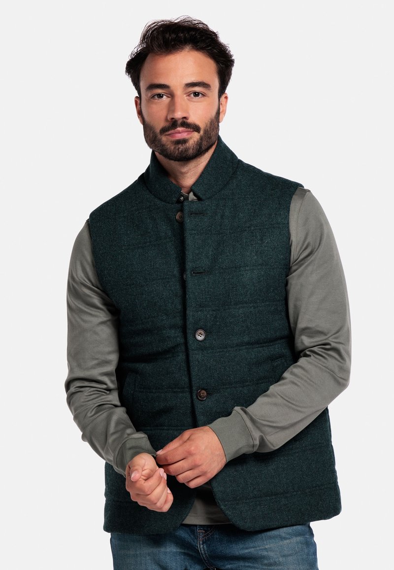 Dunkelgrüne gepolsterte Weste aus strukturiertem Stoff mit hohem Kragen und braunen Knöpfen, getragen über einem grauen Langarmshirt.