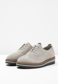 Šedé semišové boty s brogue designem, obsahující perforované detaily, šedou gumovou podrážku a vrstvenou dřevěnou mezipodešev.