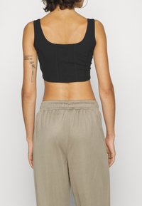 Czarny krótki top z kwadratowym dekoltem, z poziomymi szwami i dopasowanym fasonem, w połączeniu z jasnobeżowymi spodniami elastycznymi w pasie.