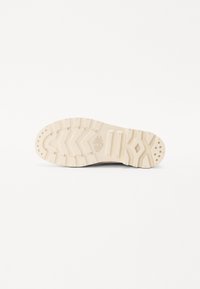 Shoe outsole in beige rubber with a textured, zigzag tread pattern and circular grip accents. Features a brand logo embossed on the heel.