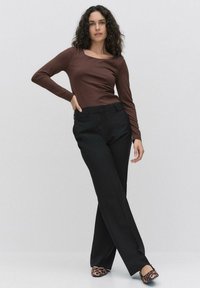 Brun långärmad topp i kombination med svarta vida byxor och flat skor med leopardmönster. Slät textur och figurnära design med rund halsringning.