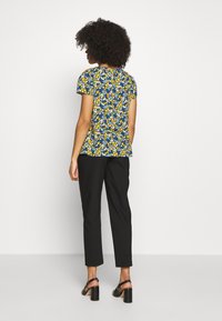Top floreale a maniche corte con sfondo blu e fiori gialli e bianchi. Abbinato a pantaloni taper neri e tacchi neri.