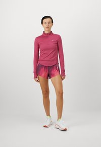 Fitte roze longsleeve top met een halve rits, gecombineerd met gradient roze sportshorts. Witte sneakers met oranje accenten maken de look compleet.