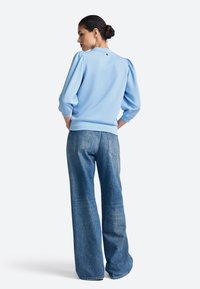 Helehall sinine pusa põlvpükste stiilis, soonikkoes käiste ja tagumise nööpdetailiga, kombineeritud kõrge vöökohaga, laiade jalgeosadega teksapükstega.