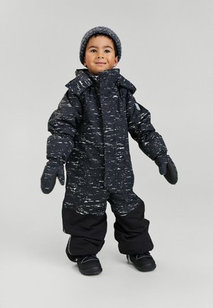 Black snow suit with white speckled pattern, featuring a hood, mittens, and loose-fitting pants. Worn with a gray knit beanie and black boots.