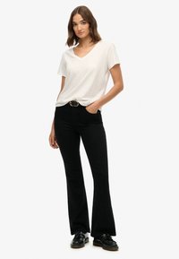 Camiseta blanca de cuello en V combinada con jeans negros acampanados de cintura alta y zapatos oxford negros, con una hebilla de cinturón redonda.