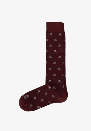 Chaussette rouge foncé avec un petit motif blanc de tête de mort et d'os croisés couvrant toute sa surface, posée à plat avec le pied étendu vers la gauche.