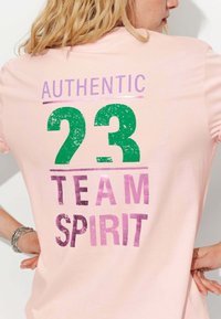 T-shirt en coton rose clair avec l'inscription "AUTHENTIC 23 TEAM SPIRIT" imprimée en vert et en rose dans des polices usées, avec une coupe décontractée.