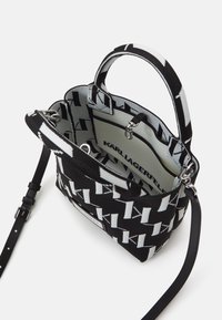 Czarna i biała pleciona torebka o strukturalnym kształcie, z wzorem logo, skórzanymi akcentami, podwójnymi uchwytami i odpinanym paskiem na ramię.
