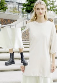 Vestido oversize beige claro con mangas cortas, combinado con botas negras hasta el tobillo con suela gruesa y acabado suave.