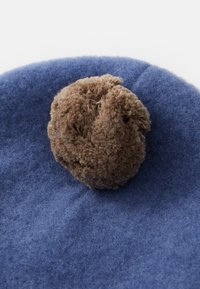 Béret en laine bleu avec un grand pompon texturé marron au centre sur le dessus, sur un fond blanc.