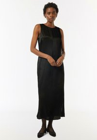 Czarna sukienka bez rękawów o prostym kroju, z delikatną teksturą, długości do kolan i bocznymi rozcięciami dla swobody ruchów.