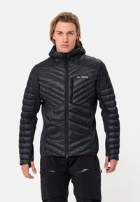 Giacca nera isolata con cappuccio, caratterizzata da un design trapuntato e sezioni lisce a contrasto. Include tasche con zip laterali e sul petto.