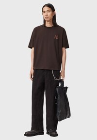 Brązowy bawełniany T-shirt z krótkim rękawem i subtelnym logo. Do tego czarne sztruksowe spodnie z dużymi kieszeniami i srebrnym łańcuszkiem.