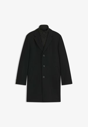 Zwarte overjas van textuurstof, met een notch-kraag, vijf knopen aan de voorkant en twee zijzakken. Gevoerd met een gewatteerd materiaal.