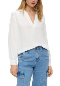 Blusa bianca a maniche lunghe con scollatura a V, realizzata in tessuto leggero. Abbinata a jeans cargo blu chiaro con tasche laterali.
