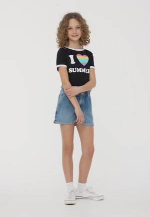 T-shirt nera con testo "I ❤️ ESTATE" e cuore arcobaleno; abbinata a pantaloni corti in denim azzurro chiaro; indossando sneakers bianche e calzini alla caviglia.