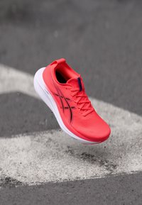 Helle rote Laufschuhe mit einer strukturierten Oberseite, schwarzen Streifen und weißer Sohle, ausgestattet mit einer Lasche an der Ferse und einem Schnürdesign.