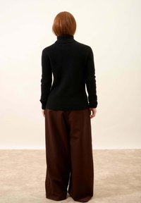 Czarny, prążkowany sweter z golfem w połączeniu z szerokimi, brązowymi spodniami. Oba elementy charakteryzują się luźnym krojem i wykonane są z miękkiego materiału.