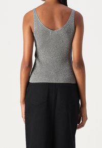 Šedé žebrované tílko s výstřihem do V na zádech, vyrobené z texturované látky a s přiléhavým střihem. Kombinováno s černou sukní s vysokým pasem.
