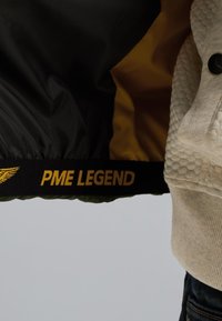 Black and yellow jacket featuring a smooth outer material, a textured cream inner lining, and a prominent "PME LEGEND" logo on the waistband.
