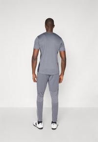 Grå treningsantrekk bestående av en tettsittende t-skjorte med korte ermer og smale bukser med kontrasterende side-striper; glatt tekstur, minimalistisk design.