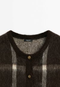 Gros plan d'un cardigan marron duveteux avec un motif à carreaux beige, encolure ronde, deux boutons dorés décoratifs et étiquette de la marque Massimo Dutti à l'intérieur du col.