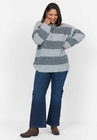 Pull rayé gris et gris clair en grosse maille avec un col rond, associé à un jean évasé bleu foncé et des bottines marron. Tissu doux et texturé.