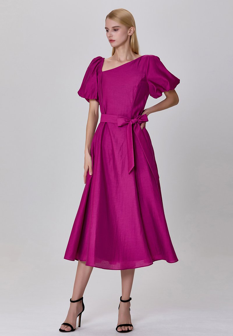 Robe fuchsia avec des manches bouffantes, un décolleté carré et un détail de taille à nouer, fabriquée dans un tissu lisse qui tombe jusqu'au mollet.