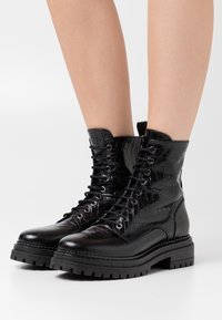 Bottes de combat à lacets noires en cuir embossé crocodile, dotées d'une semelle épaisse et d'un col rembourré pour le confort et la durabilité.