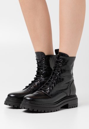 Bottes de combat à lacets noires en cuir embossé crocodile, dotées d'une semelle épaisse et d'un col rembourré pour le confort et la durabilité.