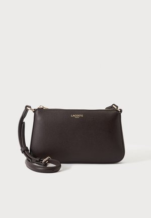 Borsa a tracolla Lacoste in pelle marrone scuro con logo dorato, chiusura con cerniera e tracolla regolabile su sfondo chiaro uniforme.