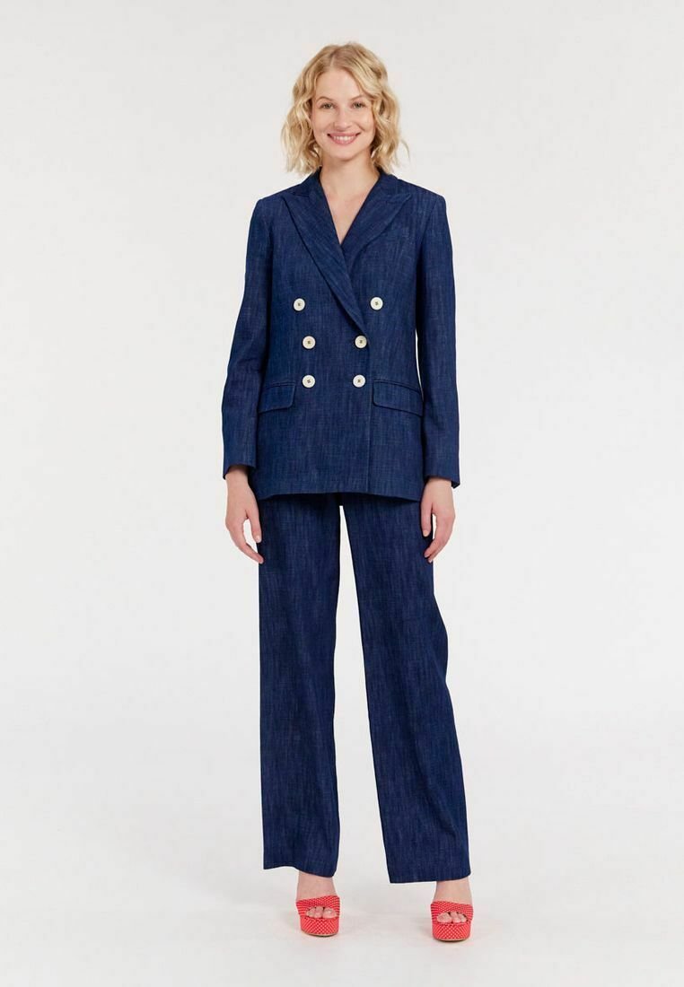 Veste croisée bleu marine à double boutonnage avec des boutons dorés et un pantalon large assorti, fabriqués en tissu en denim ; modèle portant des chaussures à plateforme rouges.