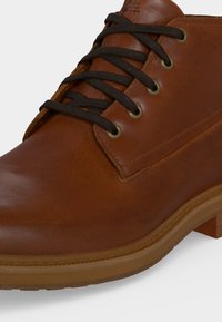 Bottine en cuir marron avec lacets noirs, œillets métalliques et semelle et talon en caoutchouc marron clair.