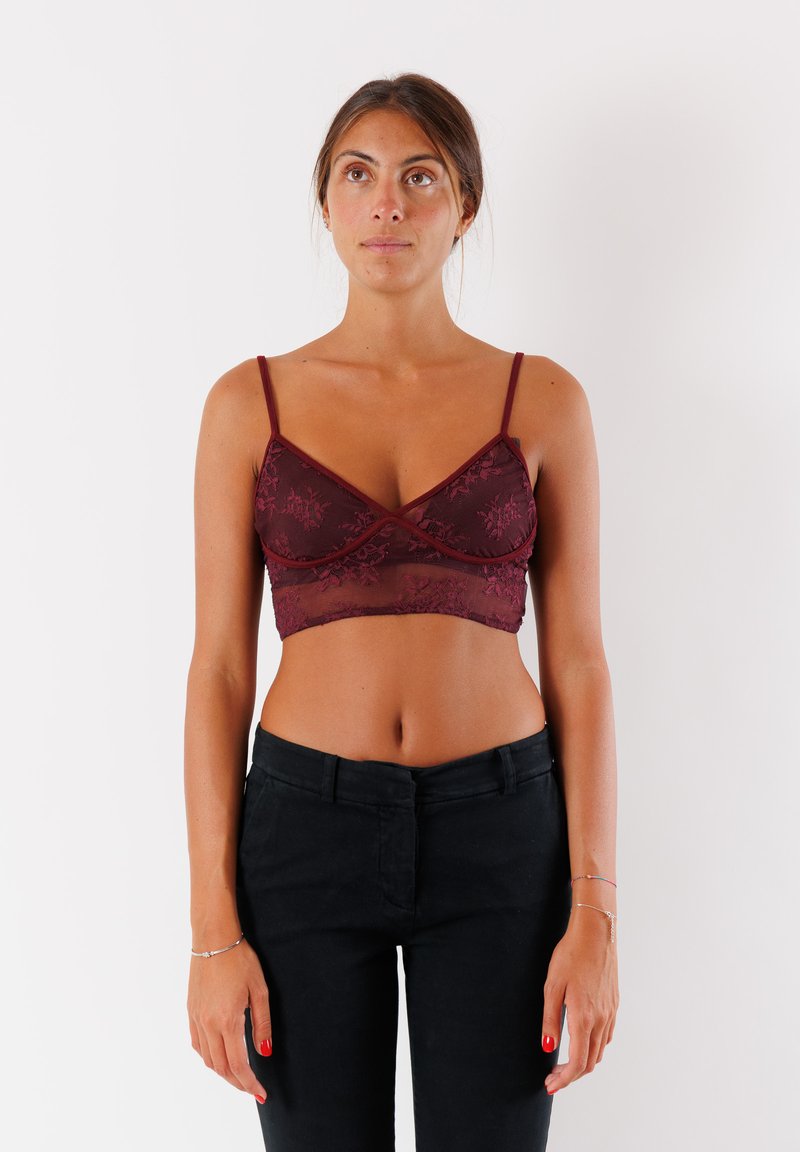 Bralette in pizzo bordeaux con spalline sottili, caratterizzato da motivi floreali e una texture morbida e leggera. Abbinato a pantaloni neri aderenti.
