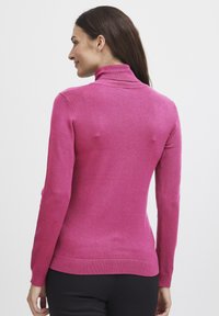Pull à col roulé magenta en tissu tricot doux, doté de manches longues, d'une silhouette ajustée et de bords côtelés aux poignets et à l'ourlet.