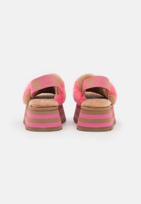 Sandály na platformě v barvě fuchsie a velbloudí kůže se chlupatým páskem nahoře, logo UGG v růžové barvě a horizontální růžové a hnědé pruhy na platformě.