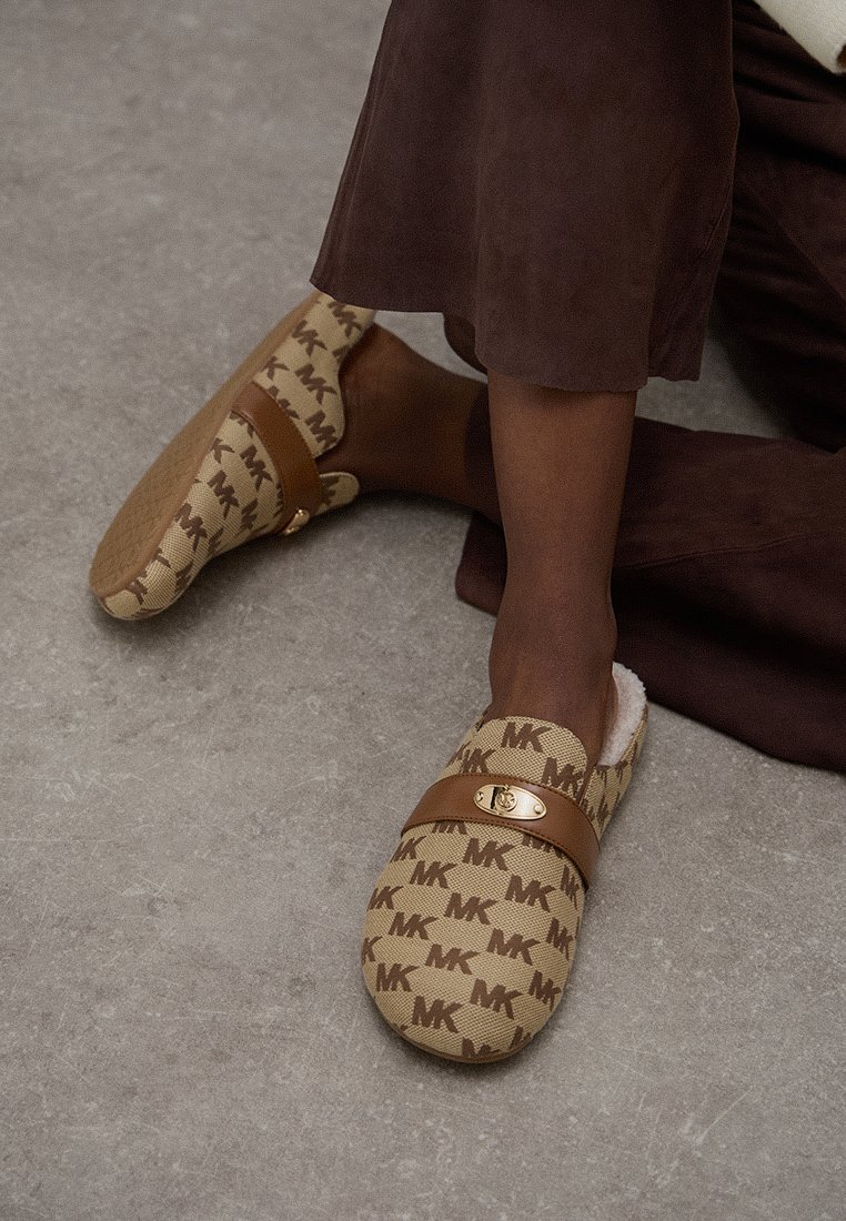 MK-märkta träskor i brunt, med en mjuk innerfoder, brun rem och mönstrad utsida. Platt, rundad form med gummisula.