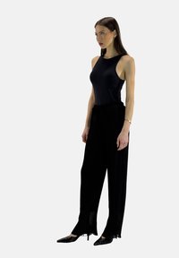 Top senza maniche nero abbinato a pantaloni plissettati neri, che mette in risalto una trama liscia e una vestibilità rilassata, completato da scarpe nere a punta.