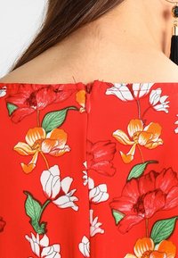 Rotes Blumenkleid mit großen gelben und weißen Blumenmotiven, einem Reißverschluss auf der Rückseite und einer glatten Stoffoberfläche.