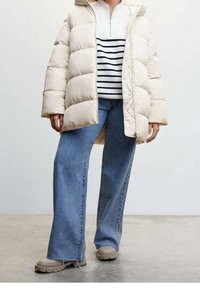 Prošívaná bunda světle béžové barvy na zip, s širokými rukávy. Pod ní bílo-námořnicky pruhovaný svetr. Kalhoty z modrého denimu s vysokým pasem a rozšířenými nohavicemi.