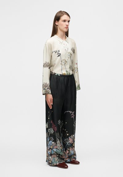 Μεταξωτό πουκάμισο με λουλουδάτο σχέδιο και γιακά, συνδυασμένο με φαρδιά μαύρη παντελόνα με πολύχρωμα βοτανικά σχέδια.