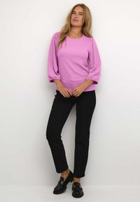 Maglione a maglia testurizzata rosa con maniche a sbuffo, abbinato a pantaloni neri aderenti e mocassini neri con dettagli in oro.