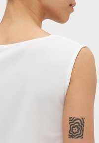 Witte mouwloze top met een gladde textuur. Beschikt over een bootnek en een zichtbare bloemtattoo op de bovenarm.