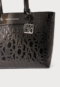 Μαύρη τσάντα tote με ανάγλυφο σχέδιο λογότυπου, γυαλιστερή υφή, λεπτομέρεια ασημένιων εξαρτημάτων, έντονη εταιρική ταυτότητα, ανθεκτικές λαβές.