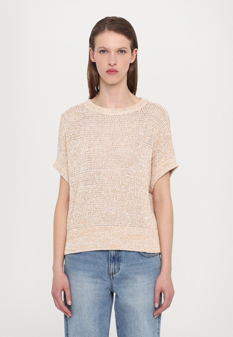 Lyserød strikket sweater med korte ærmer, rund halsudskæring og løs pasform, parret med lyseblå denimjeans.