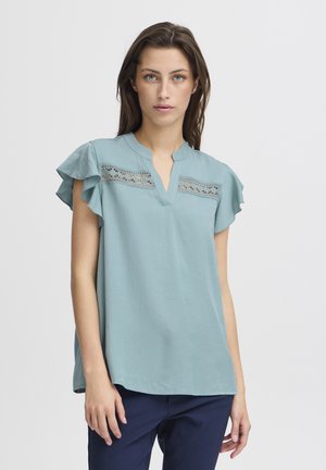Blouse à manches courtes bleu clair avec décolleté en V, détails en dentelle sur la poitrine et manches à volants. Tissu doux avec une coupe décontractée.