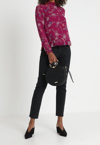 Vinröd blus med långärmar och blommönster, svarta tajta jeans och rund svart handväska med gulddetaljer och handtag, matchat med svarta högklackade skor.